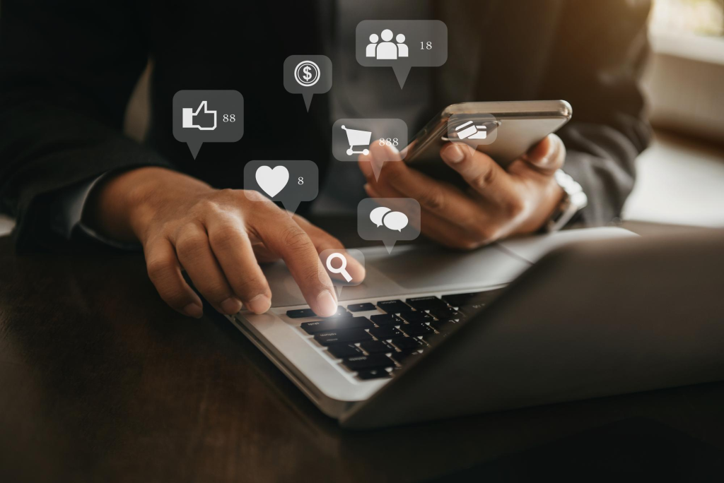 Manos sobre portátil y smartphone, iconos de redes sociales.