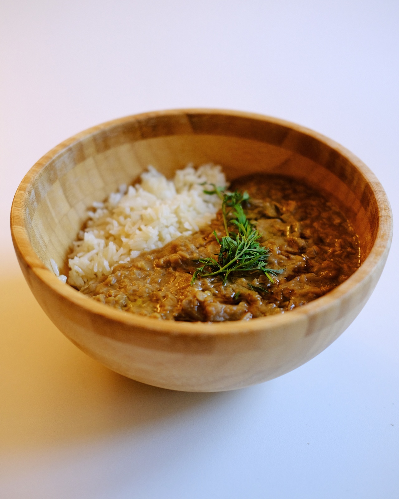 Lentil-aubergine-pomegranate stew served with rice in wooden bowl, in my kitchen in Amsterdam, 2021.