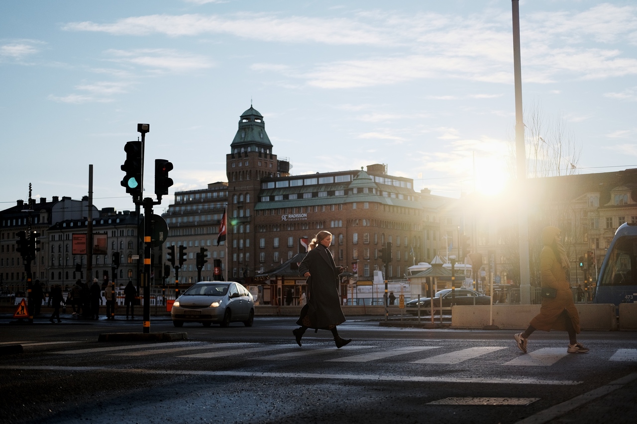 A woman floating above a street crossing in Stockholm with the sun flaring through the city's buildings.