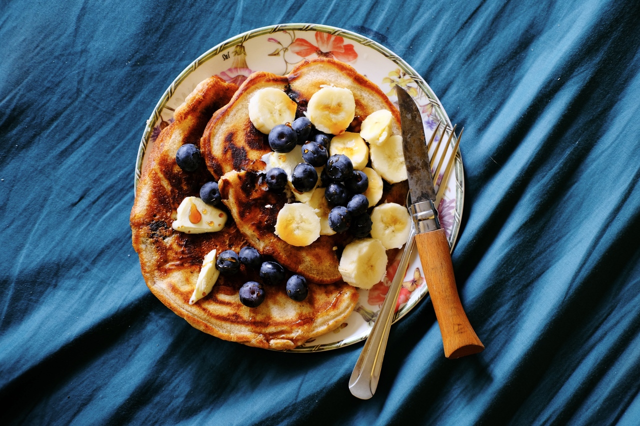 A plate of stacked pancakes with blueberries and bananas, with syrup drizzled over top. In Noemi's apartment in Amsterdam, 2022